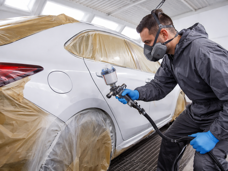 A man is spraying a white car in a spray booth following repairs