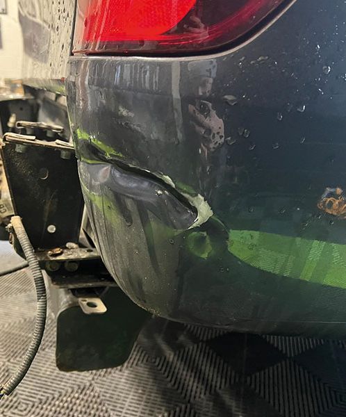 A damaged car bumper with a large whole and dent is being fixed by a technician at Them Paint Guys