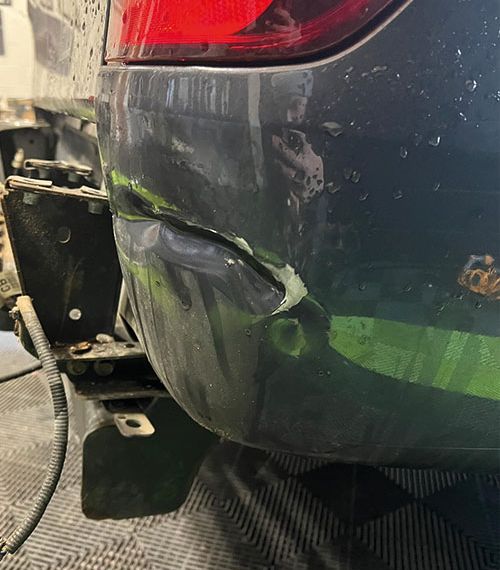 A damaged car bumper with a large whole and dent is being fixed by a technician at Them Paint Guys