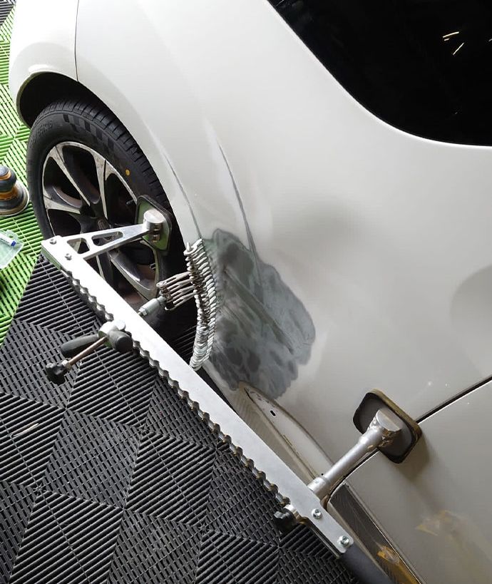 A white vehicle is being dent pulled to repair damage to the wing. 