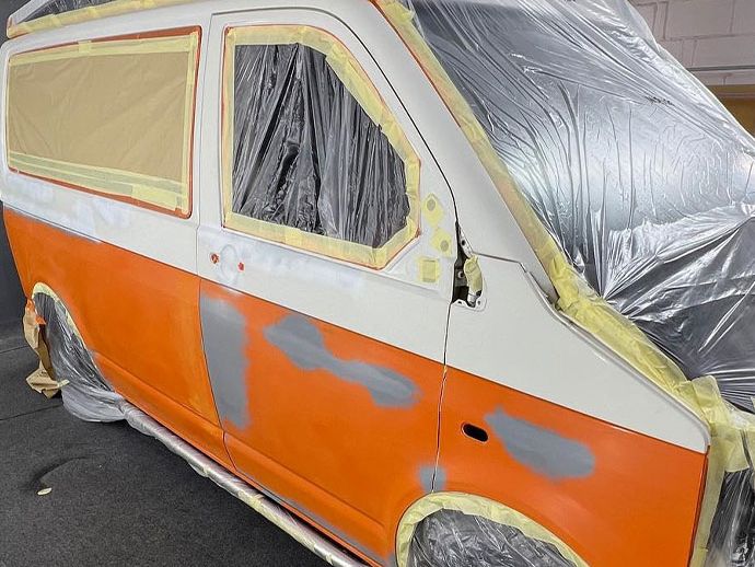 An orange and white van is in the process of being painted, following damage repair.