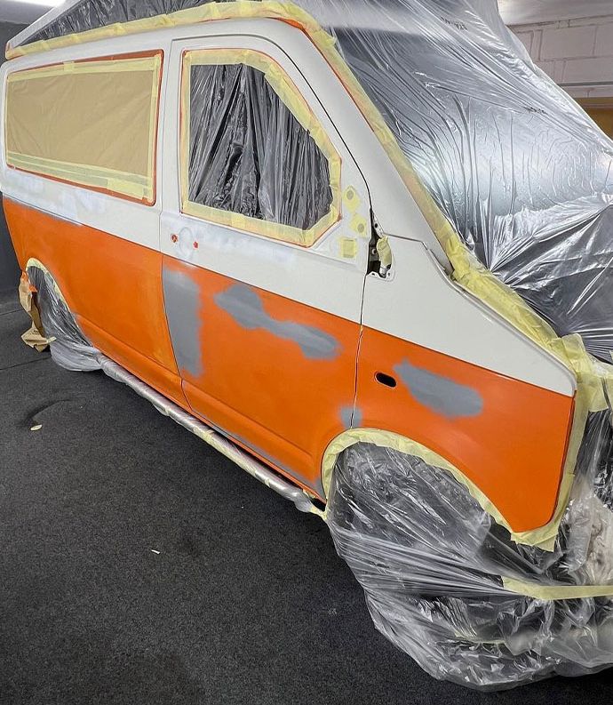 An orange and white van is in the process of being painted, following damage repair.