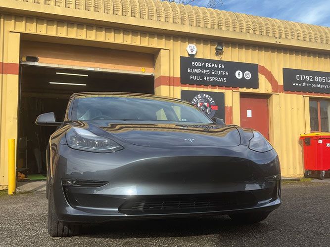A grey Tesla Model 3 parked in front of Them Paint Guys bodyshop following cosmetic repairs being completed. 